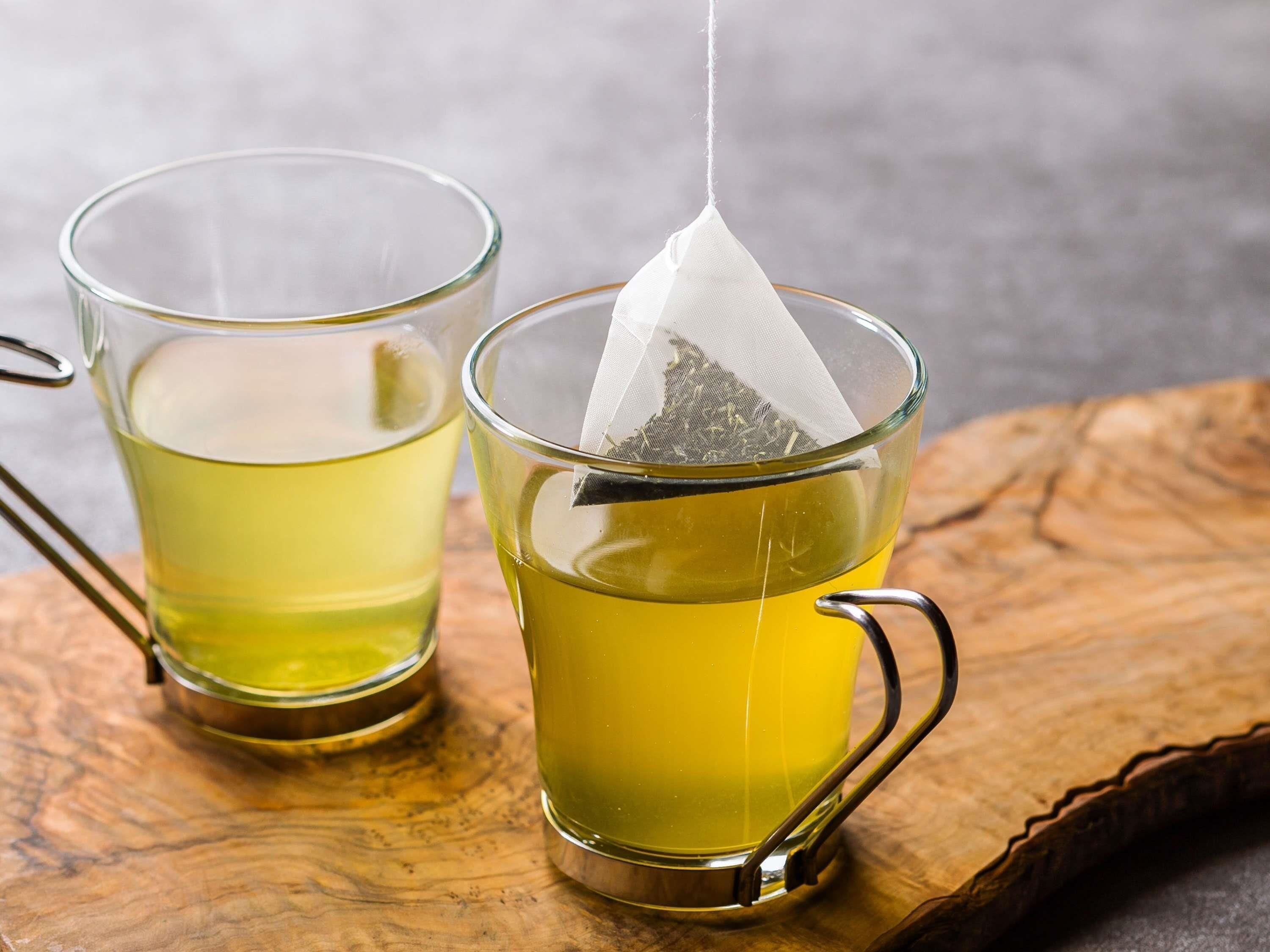 Dos tazas de vidrio con asa, una con una bolsita de té, sobre una superficie de madera.