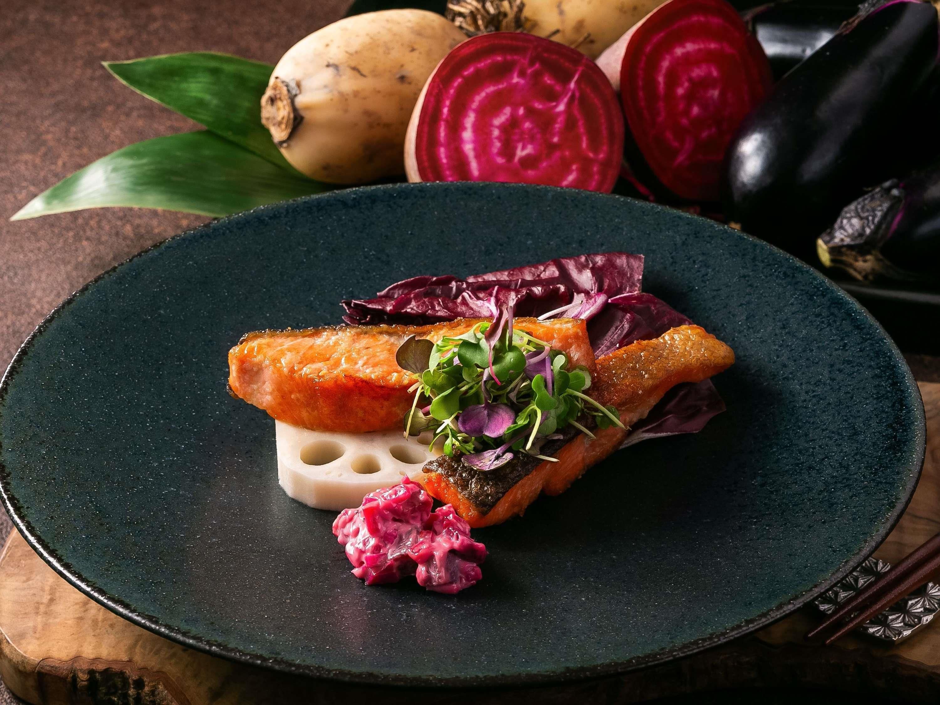 Un plato con salmón, remolacha y verduras sobre un plato oscuro.