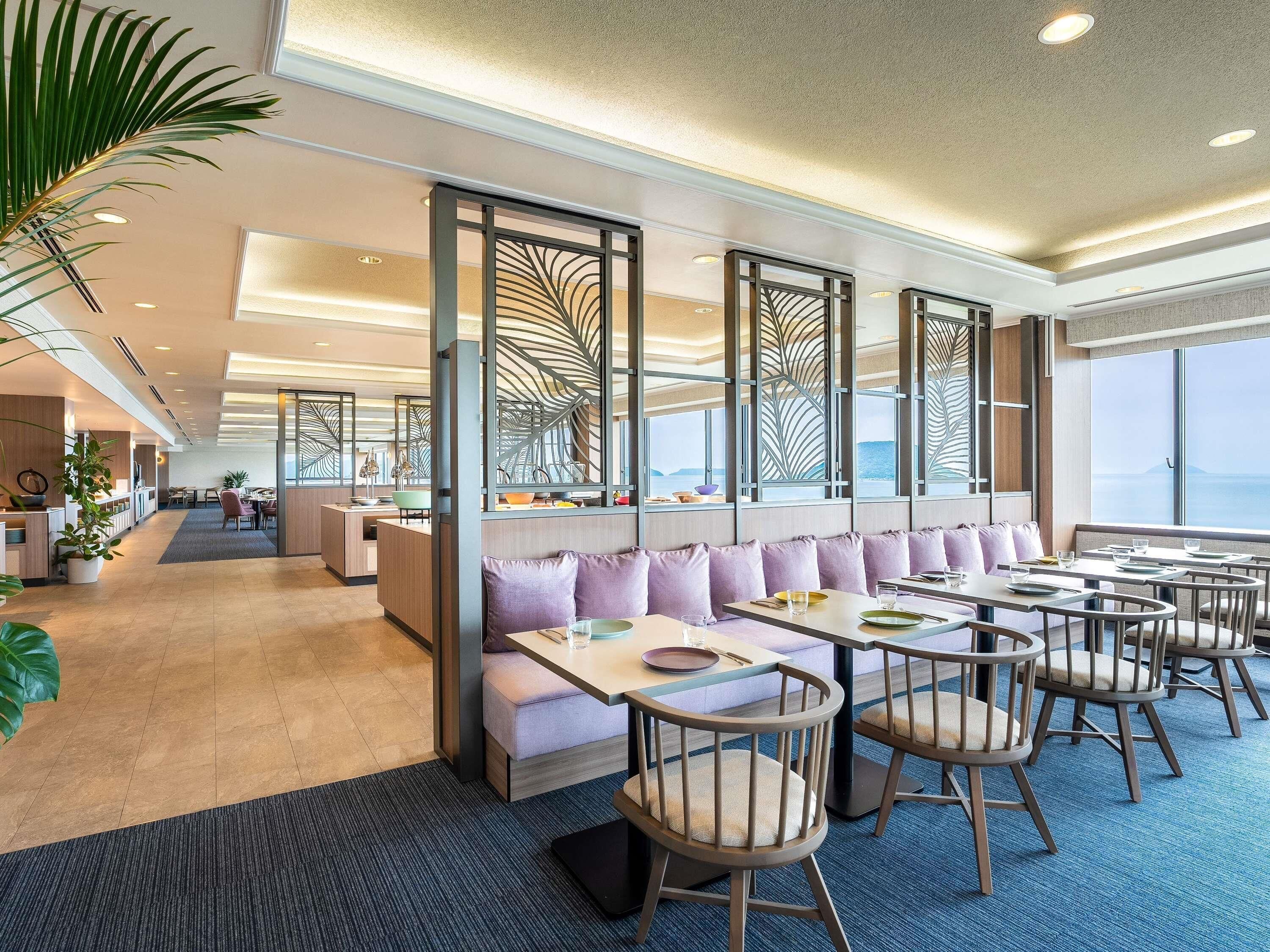 A modern dining area with high tables and cushioned seating, large windows with a view, and decorative partitions.