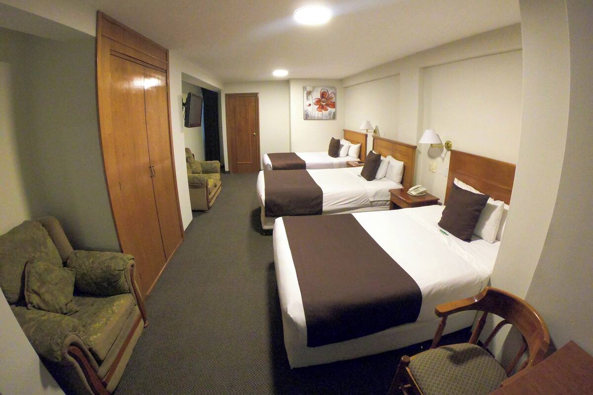 Et hotelværelse med to senge, en sofa, en stol og et skrivebord med telefon.