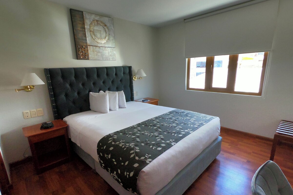 A hotel room with a large bed, two bedside tables, a window, and a wall-mounted artwork.