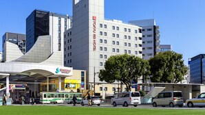 Ein modernes Hotel mit einem gut sichtbaren Schild mit der Aufschrift "TOKYU REI HOTEL", einem überdachten Eingang und einer Straßenbahn in der Nähe.