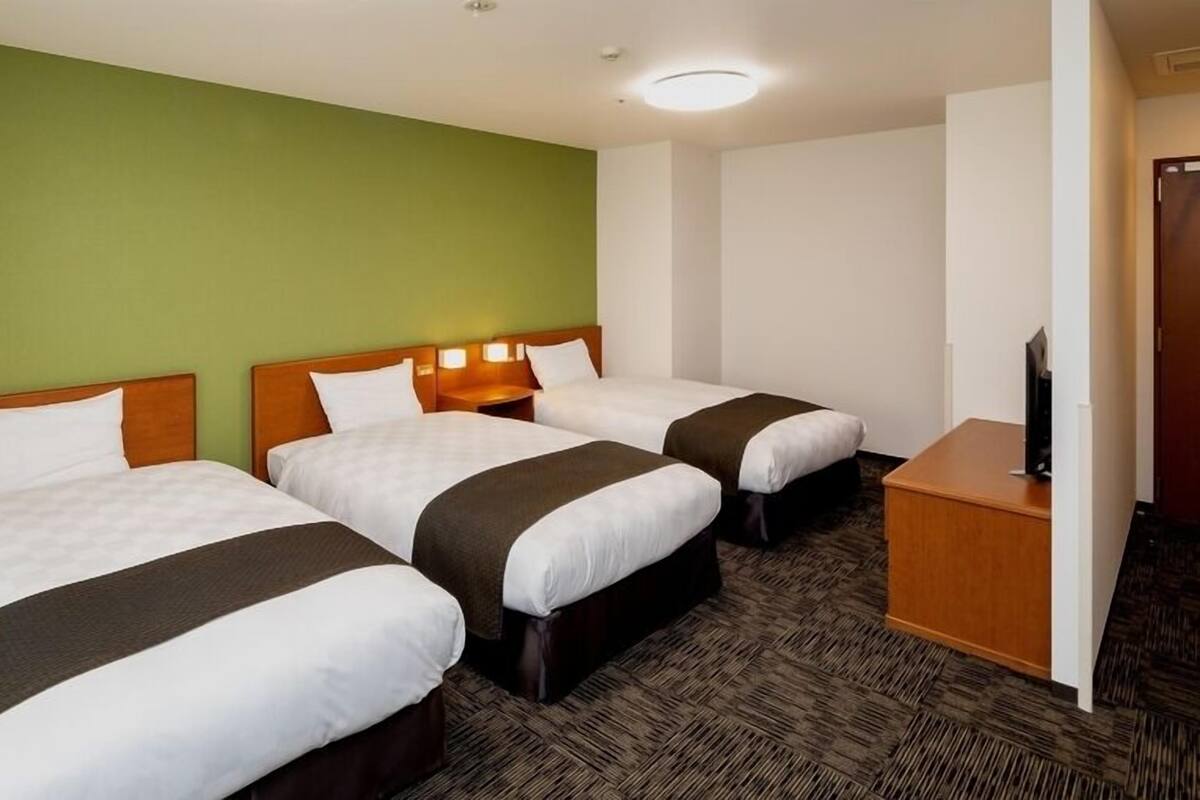 A hotel room with three beds, a television, and a green wall.