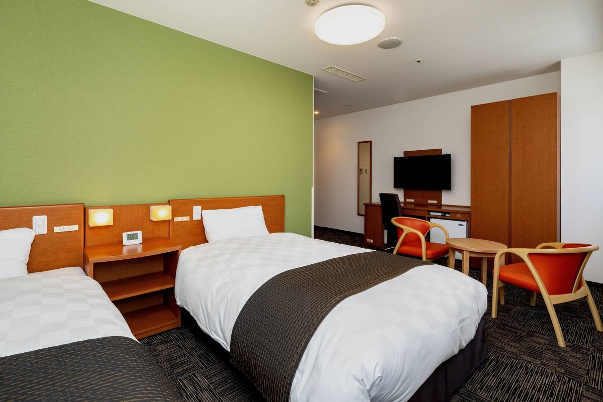 A hotel room with two beds, a desk, a chair, and a television.