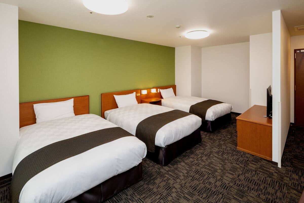 A hotel room with two beds, a wooden nightstand, and a television.