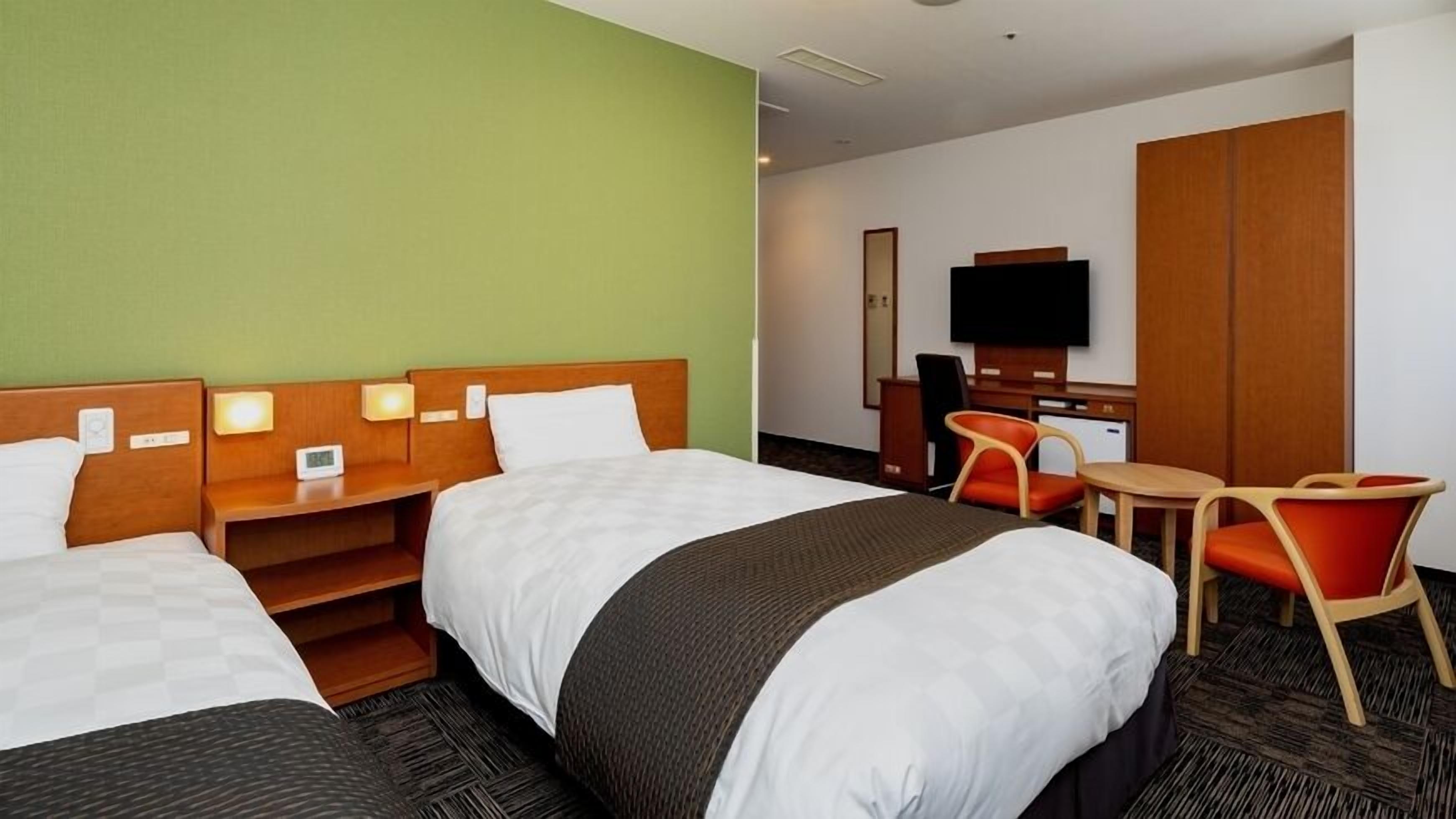 Ett hotellrum med två sängar, ett skrivbord, en stol, en tv och en garderob.