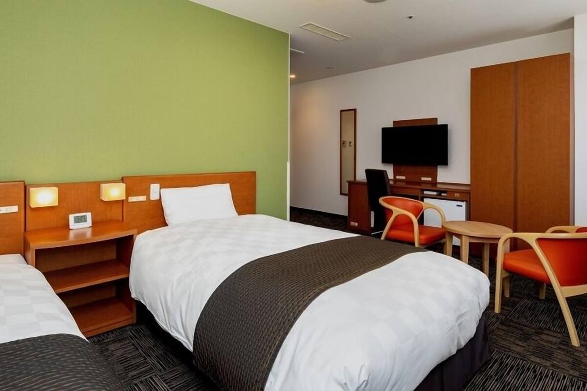 A hotel room with two beds, a desk, a chair, a television, and a wardrobe.