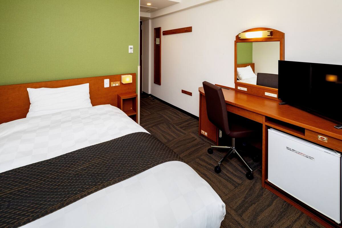 A hotel room with a bed, a desk, a television, and a mini-fridge.