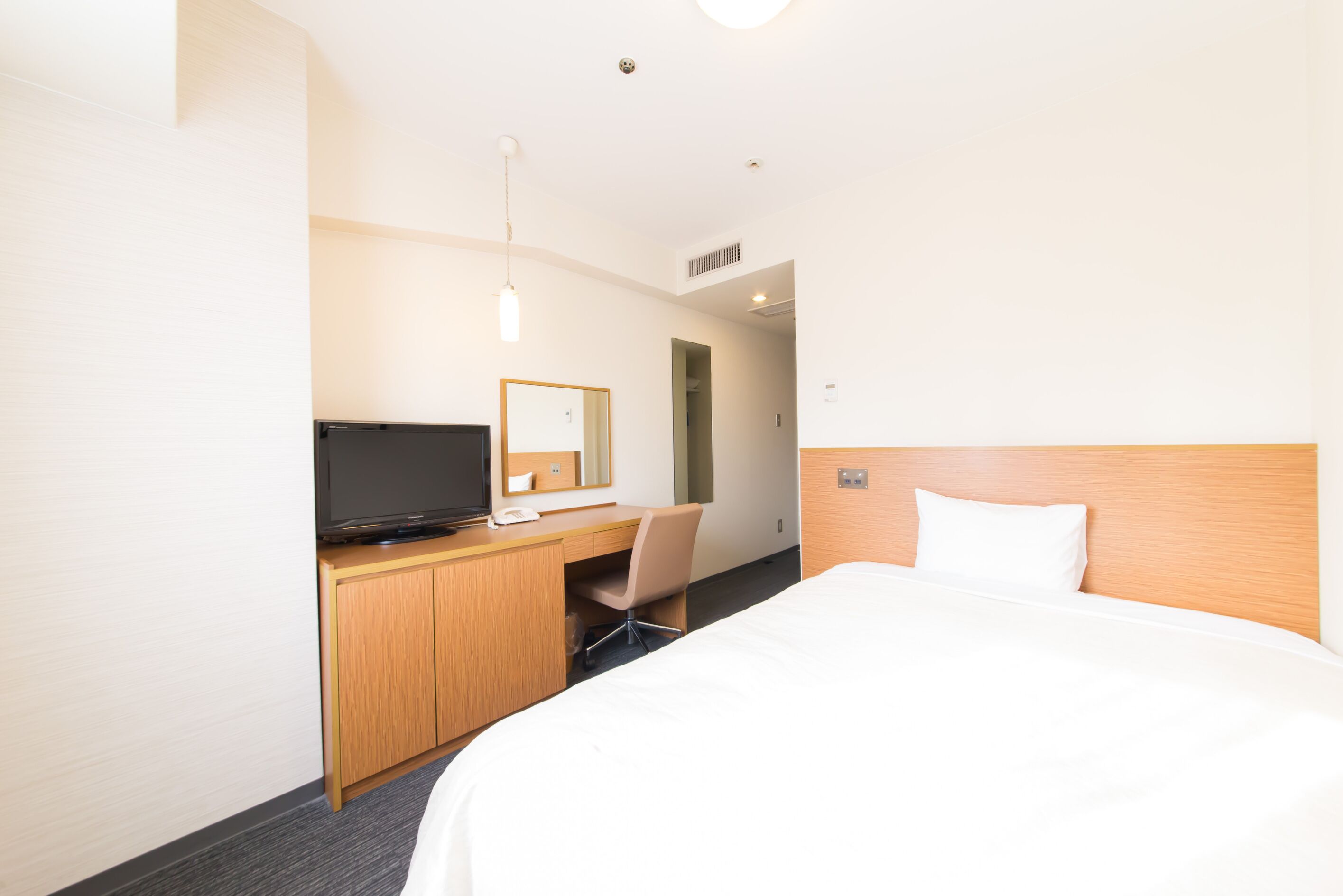 Ein Hotelzimmer mit einem Bett, einem Schreibtisch mit Fernseher, einem Sessel und einem Spiegel.