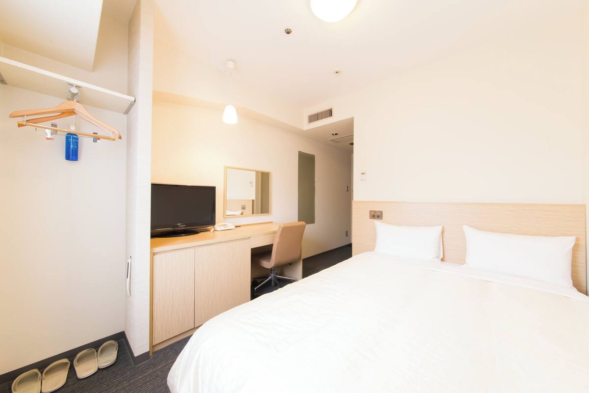 A hotel room with a bed, a desk with a chair, a television, and a mirror.