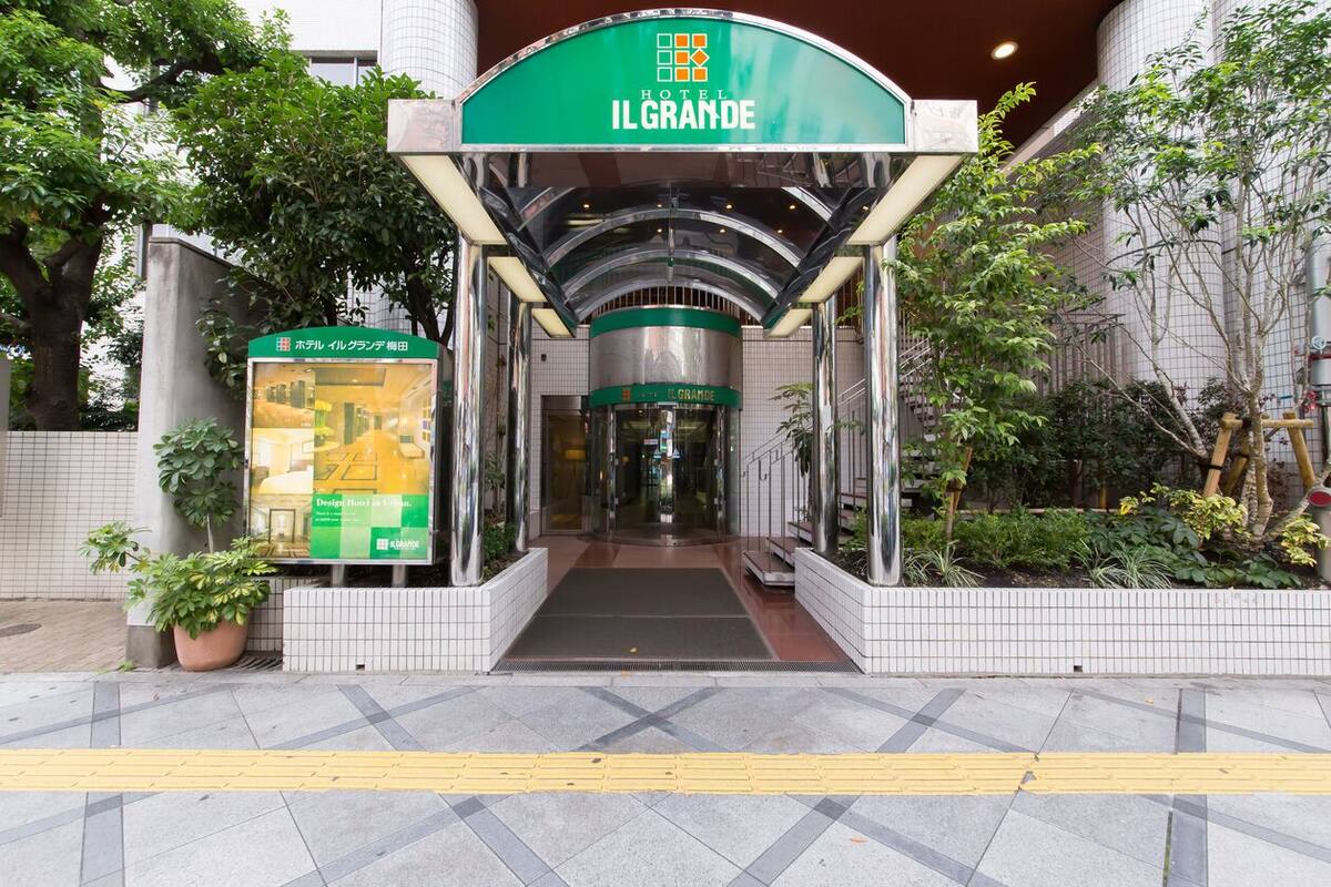 The entrance to Hotel Il Grande with a green and white facade, a tiled pathway, and potted plants.