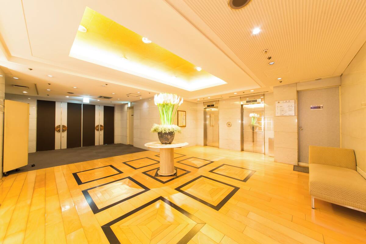 A hotel lobby with a polished wooden floor, a central round table with a potted plant, and a sofa.