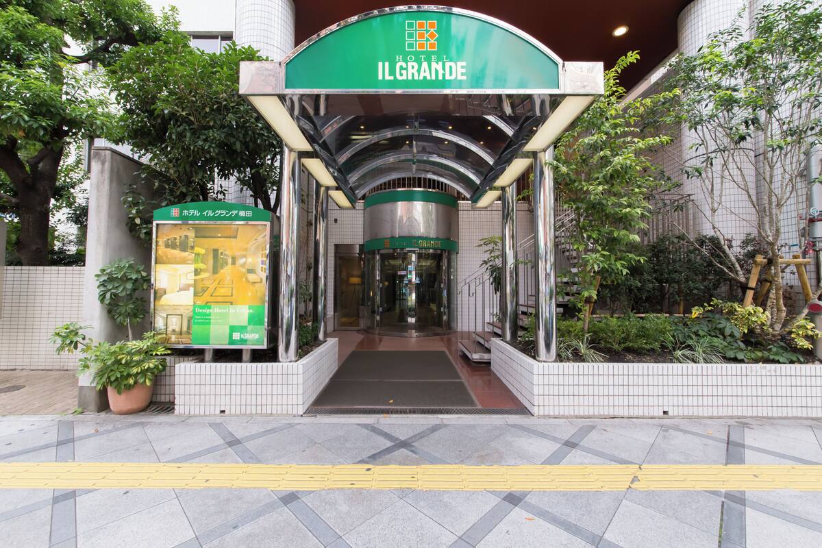The entrance to Hotel Il Grande with a green awning, tiled flooring, and potted plants.