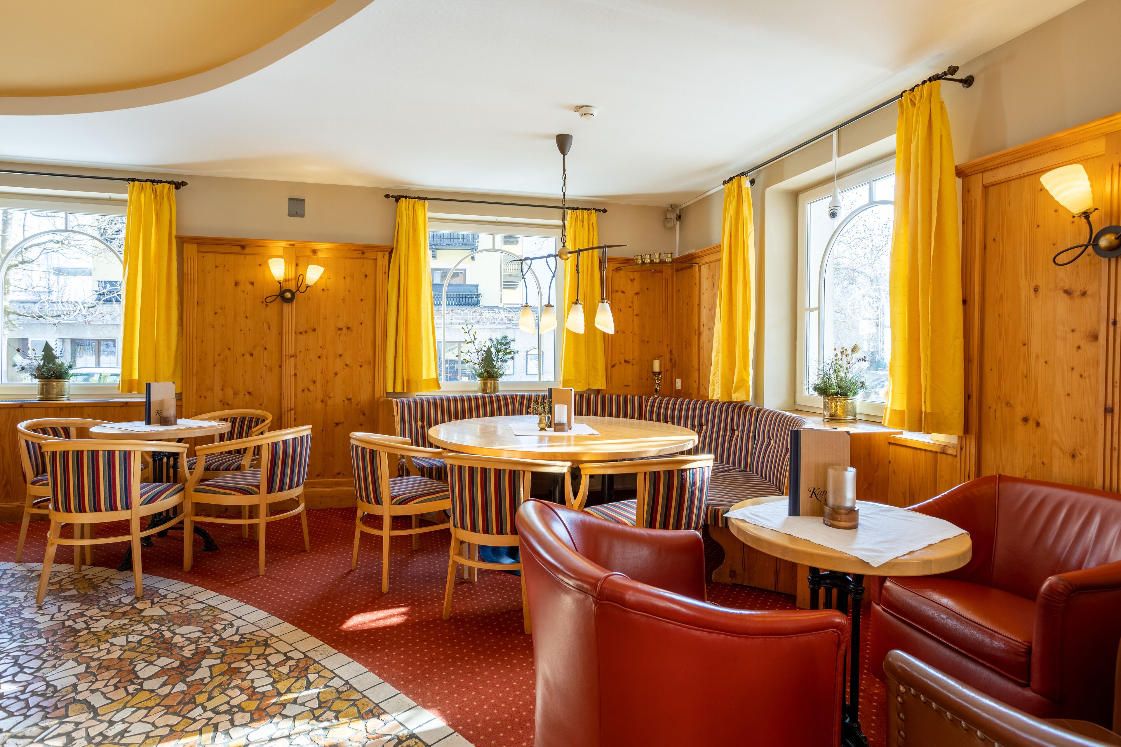 Un coin repas accueillant avec une table ronde, des chaises à rayures, un canapé en cuir rouge et des rideaux jaunes.
