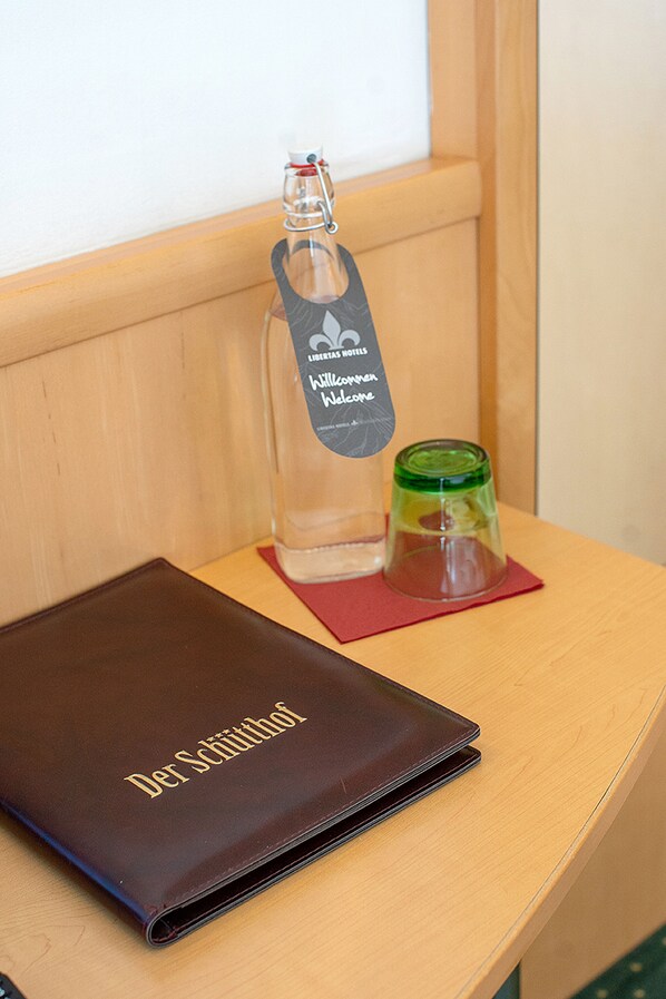 A wooden table with a brown leather folder labeled "Der Schüttkopf," a clear glass bottle with a metal clasp, and a green glass container. - Hotel Der Schütthof (Zell am See)