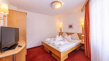 Quarto de hotel com cama, televisão, escrivaninha e tapete vermelho com bolinhas.