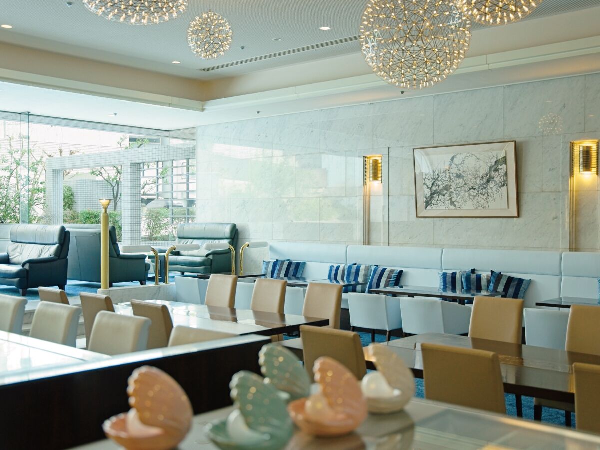 A modern hotel lobby with seating areas, a reception desk, and a large window offering a view of the outdoors.