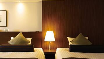 Una camera d'albergo con due letti, un comodino con una lampada e una testiera in legno.