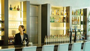 Una zona de bar con un cantinero, una barra alargada y estantes llenos de botellas de licores.