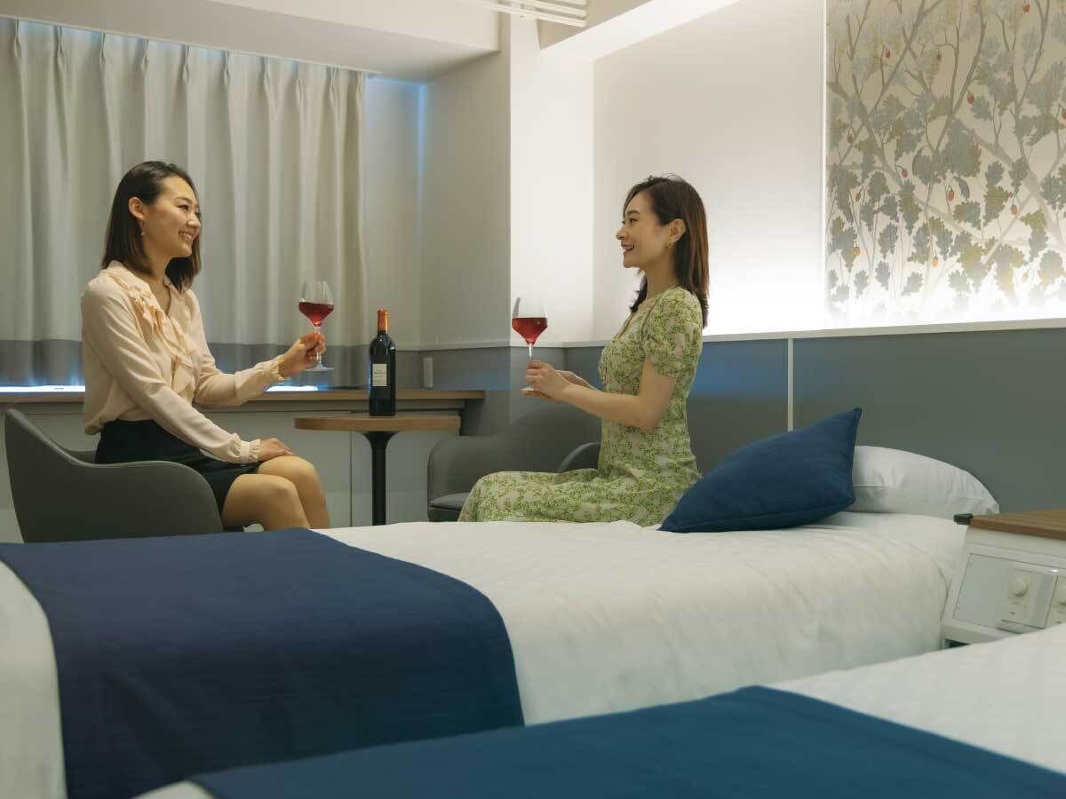 Habitación de hotel con dos camas, una zona de estar y una mesa con copas de vino y una botella.