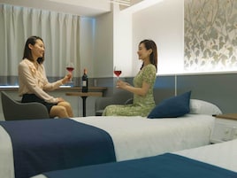 A hotel room with two beds, a sitting area, and a table with wine glasses and a bottle.
