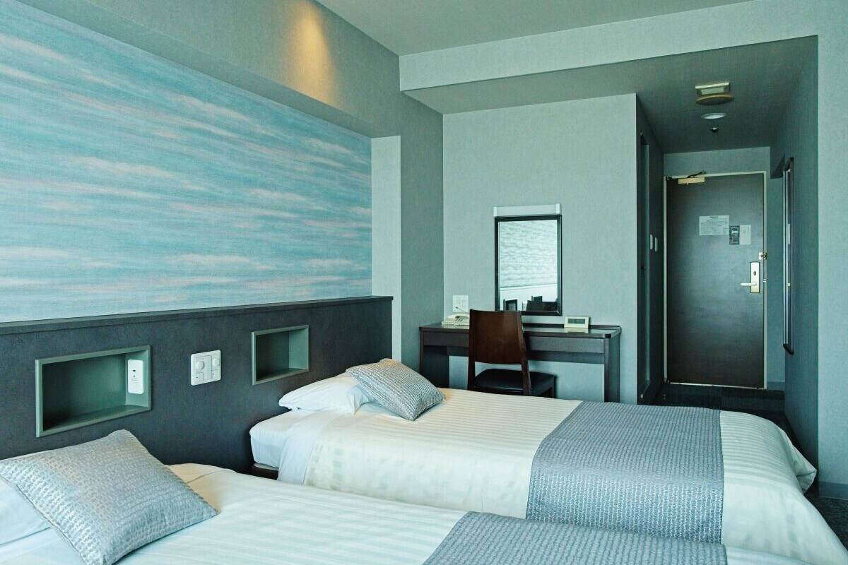 Habitación de hotel con dos camas, un escritorio, una silla y una puerta.
