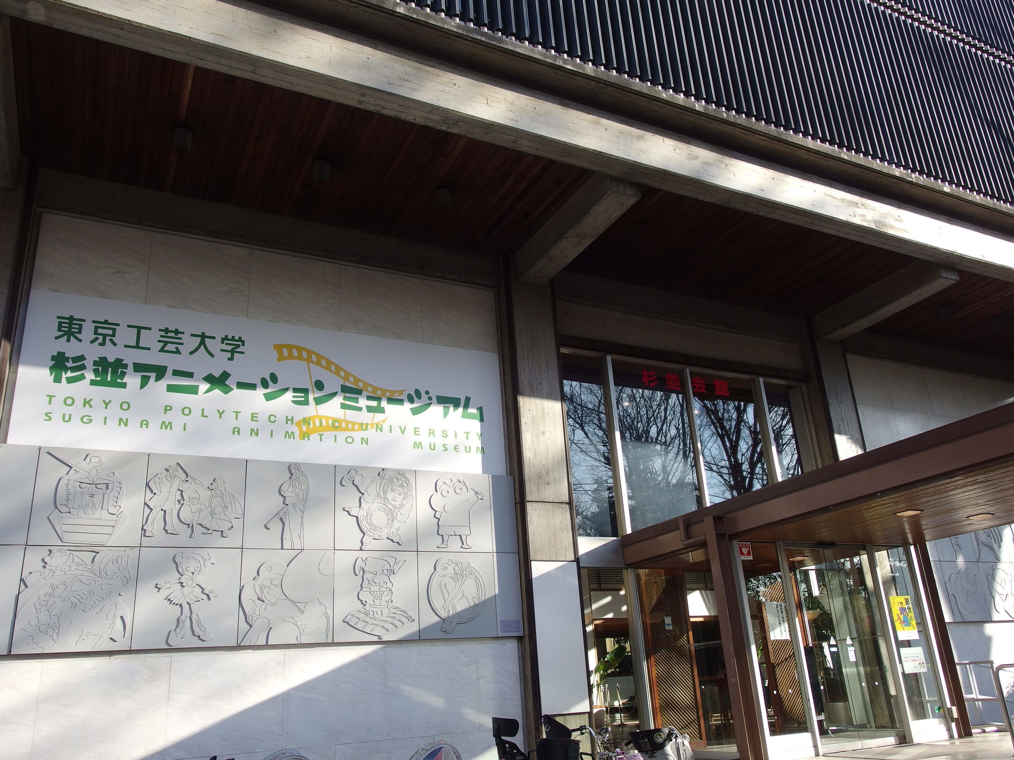 The entrance of Tokyo Polytechnic University Suginami Animation Museum with a large sign and various artistic sketches on the wall.