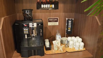 A self-service coffee station with a coffee machine, cups, and a sign indicating operating hours.