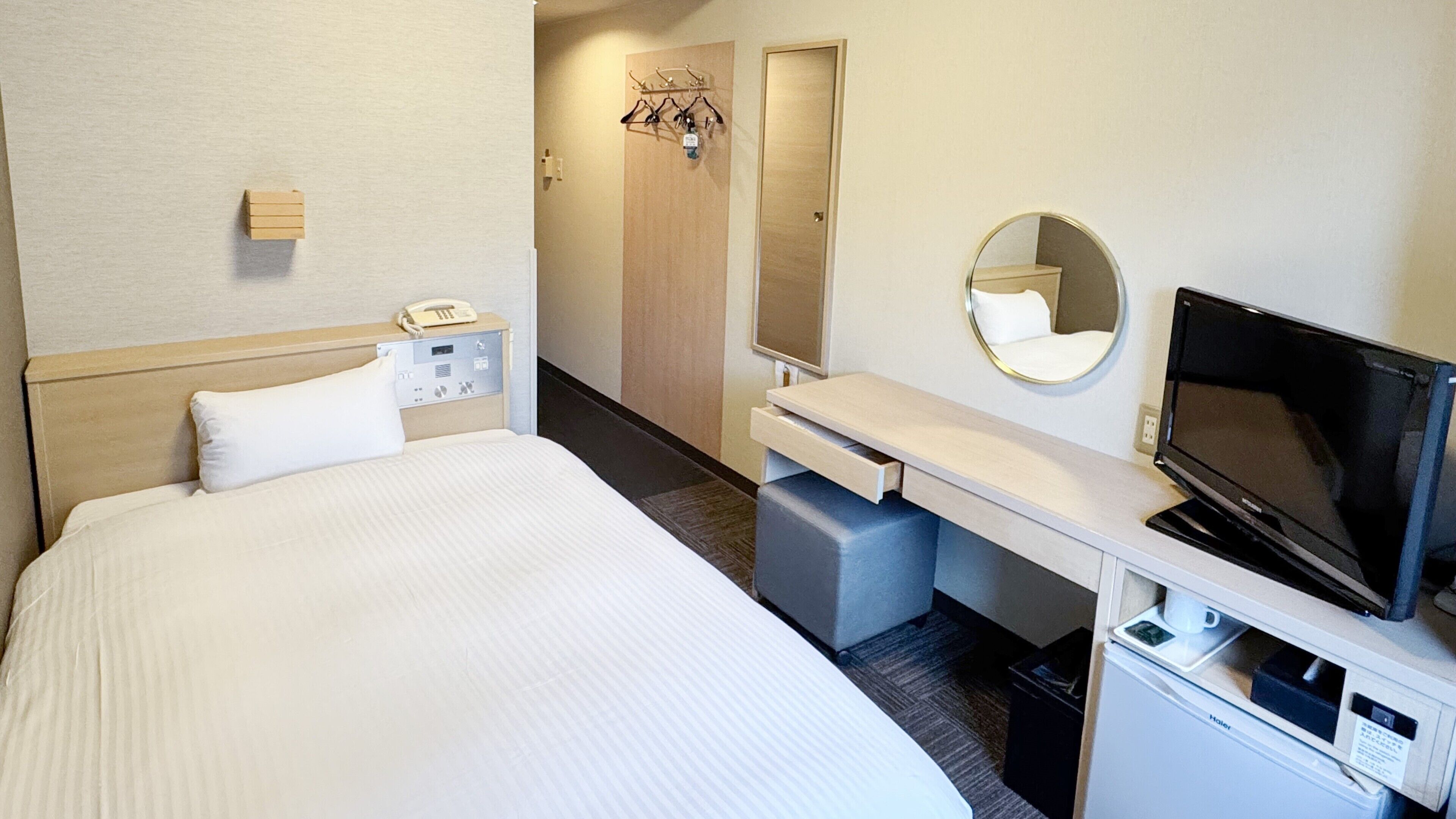 Une chambre d’hôtel équipée d’un lit, d’un téléphone sur la table de chevet, d’une télévision, d’un bureau, d’un miroir et d’un porte-manteau avec des cintres.