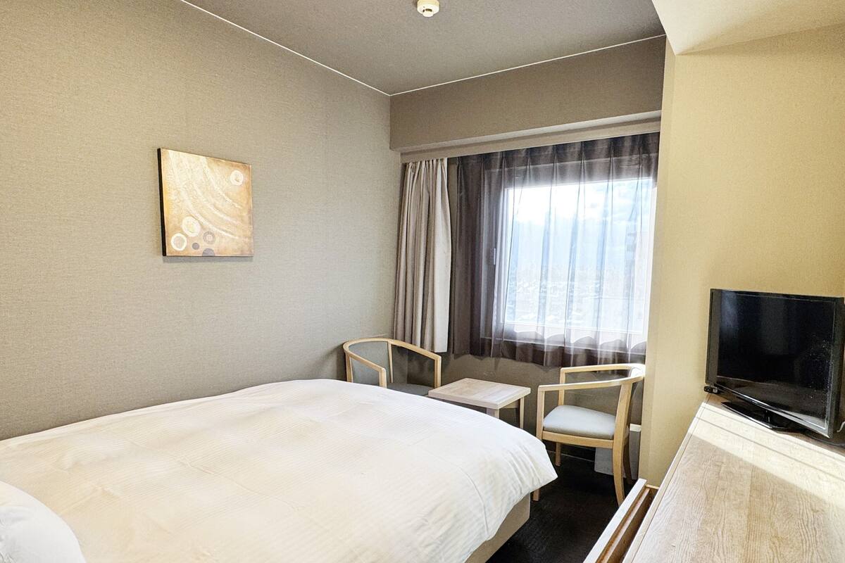 Una camera d'albergo con un letto grande, una scrivania, una sedia, un televisore e una finestra con tende.