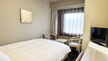 Een hotelkamer met een groot bed, een bureau, een stoel, een televisie en een raam met gordijnen.
