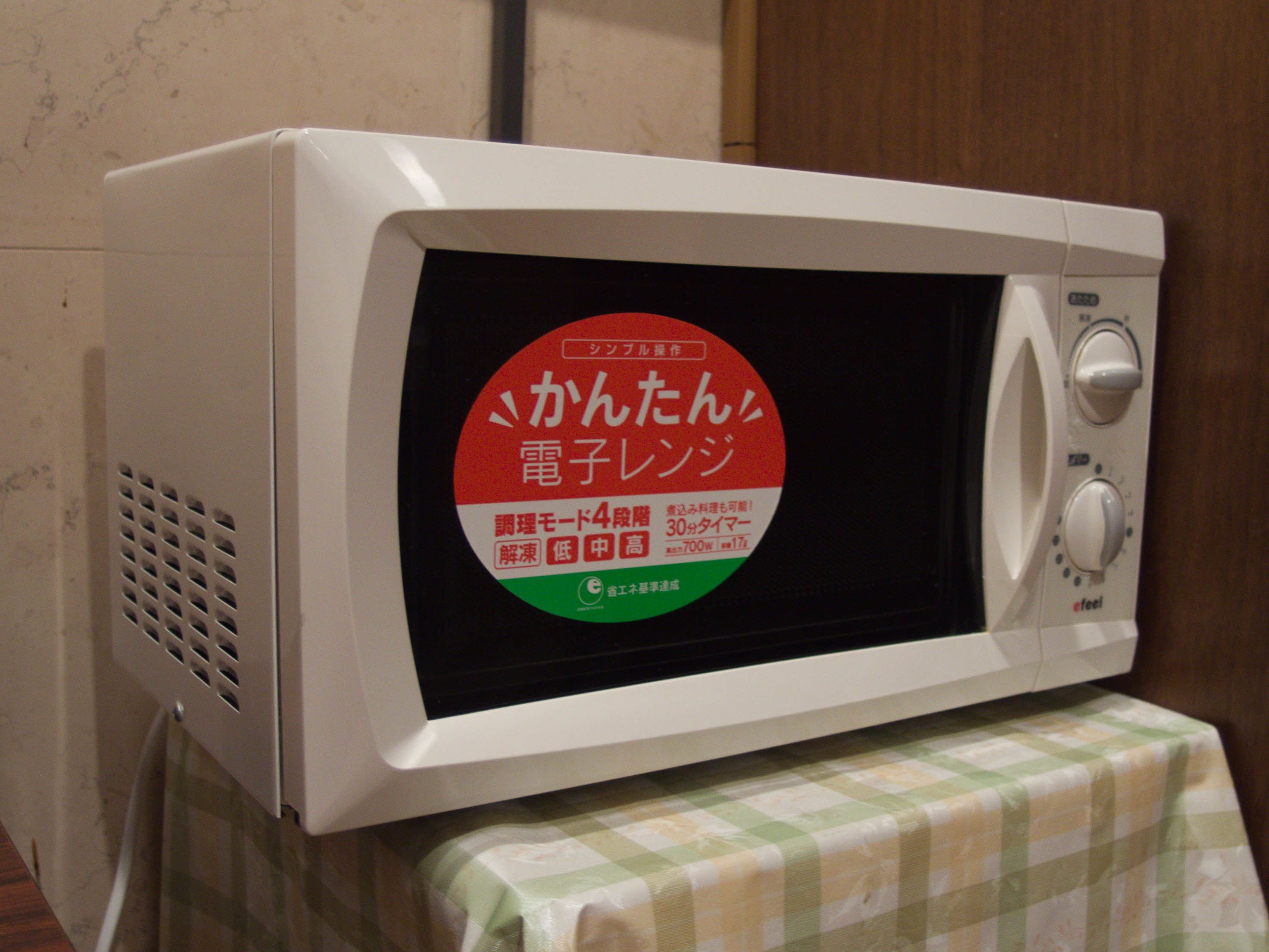 Eine Mikrowelle mit japanischem Text auf dem Bildschirm, auf einem Tisch mit kariertem Tischläufer platziert.