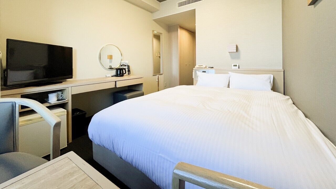 Une chambre d’hôtel équipée d’un lit, d’un bureau avec une télévision, d’une chaise, d’une machine à café et d’un miroir.