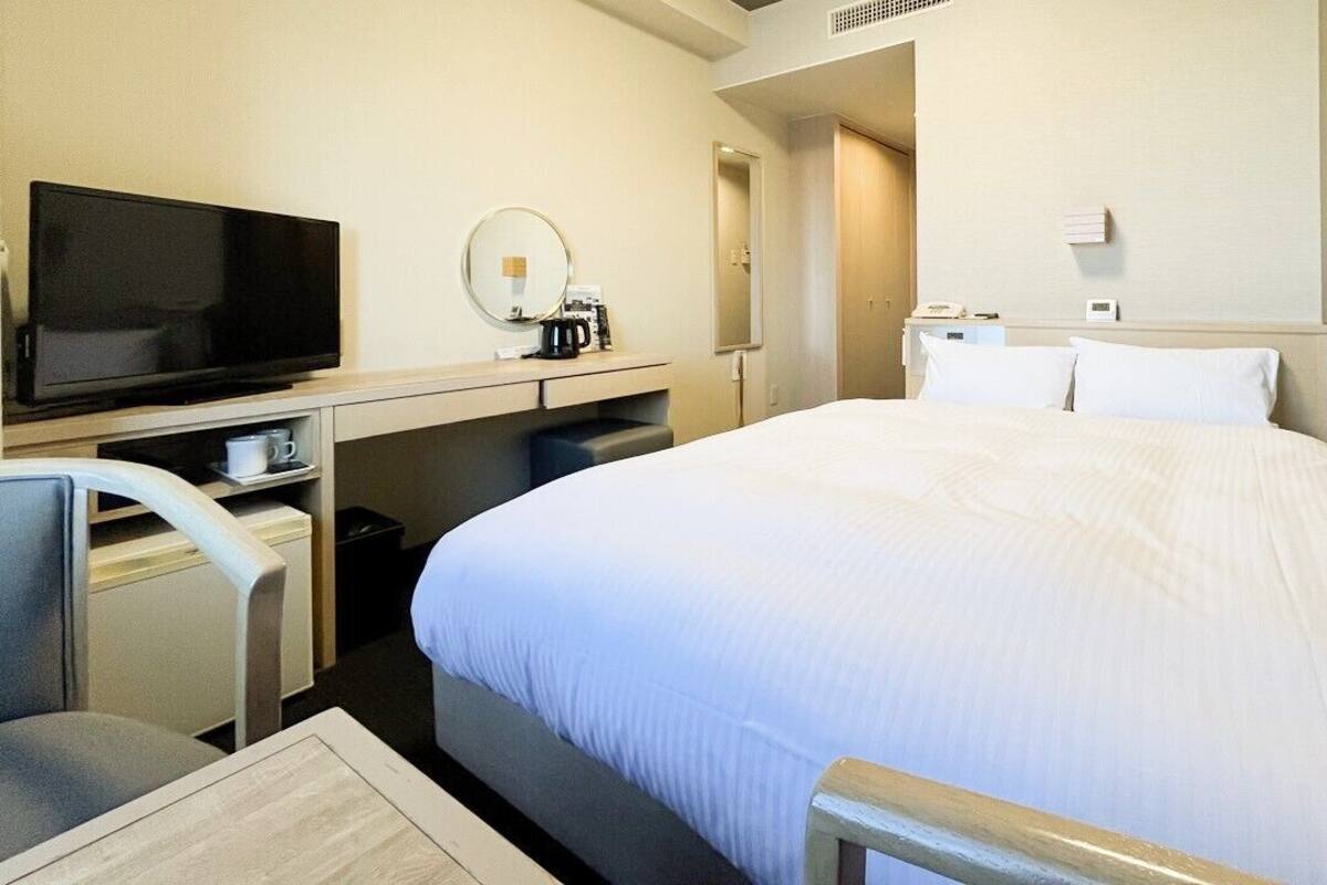 Camera d'albergo con un letto, una scrivania con televisore, una sedia, una macchina per il caffè e uno specchio.