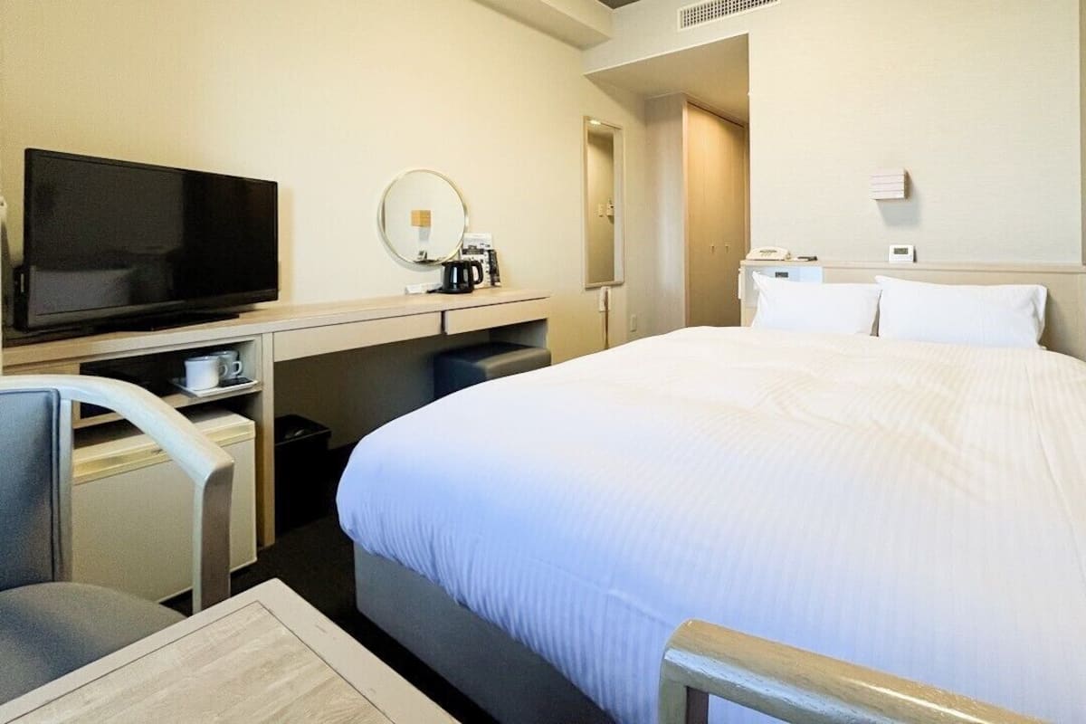 Une chambre d’hôtel équipée d’un lit, d’un bureau avec une télévision, d’une chaise, d’une machine à café et d’un miroir.