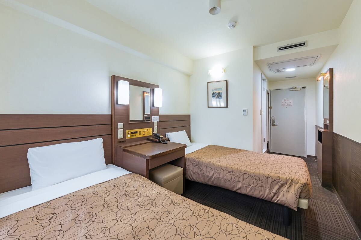 Habitación de hotel con dos camas, un escritorio, un espejo y una puerta que da a un baño.