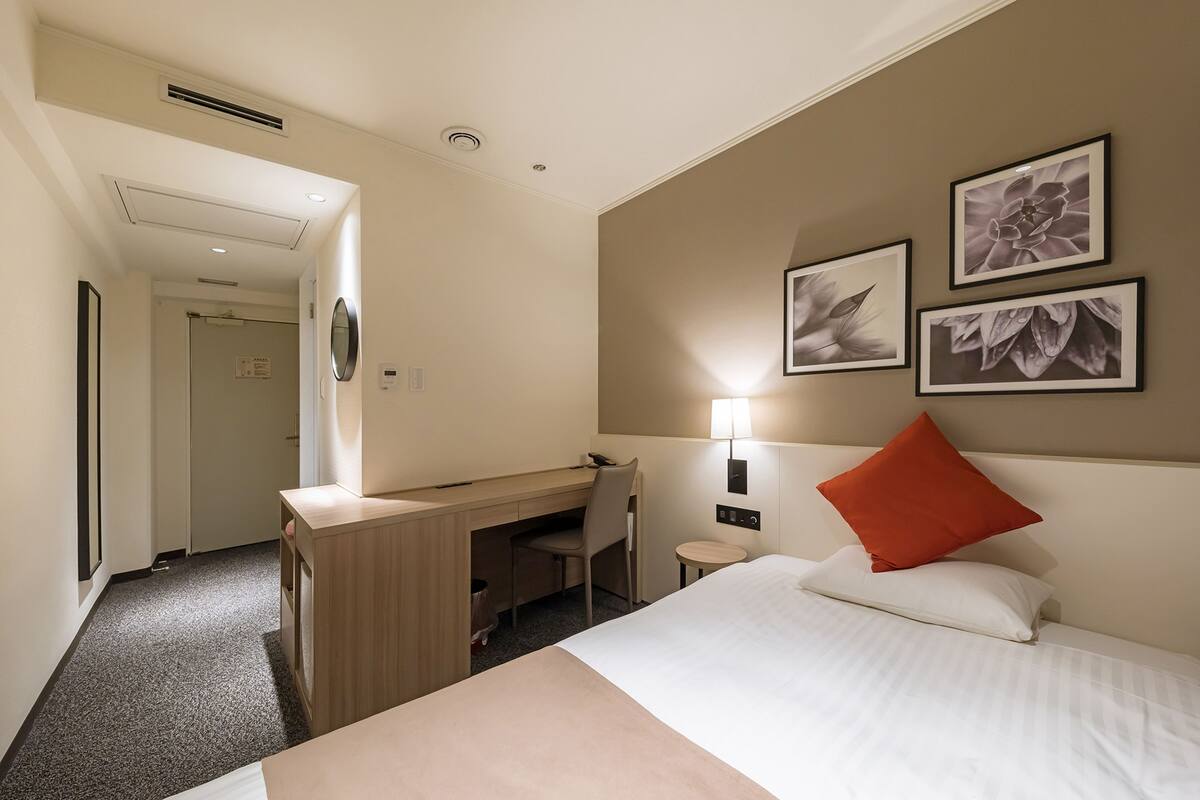 Una habitación de hotel con cama, escritorio, silla y una obra de arte colgada en la pared.