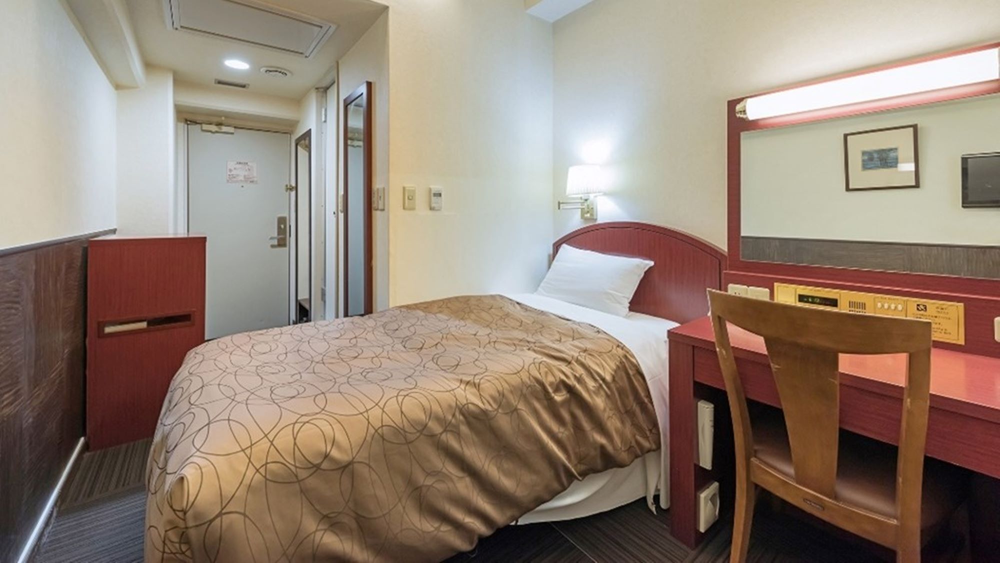 A hotel room with a bed, a desk, a chair, a mirror, and a door.