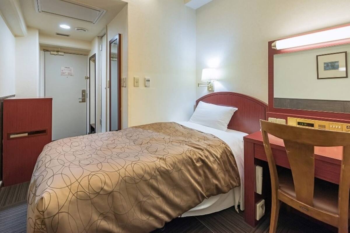 Habitación de hotel con cama, escritorio, silla, espejo y puerta.