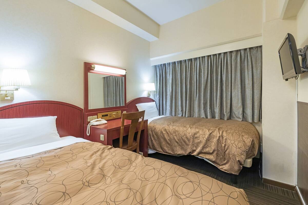 Habitación de hotel con dos camas, un escritorio, una silla, un teléfono y un televisor fijado a la pared.