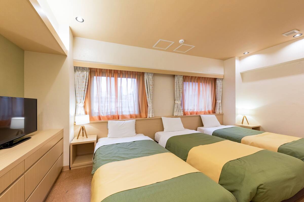 Habitación de hotel con dos camas, un televisor, un escritorio y cortinas.