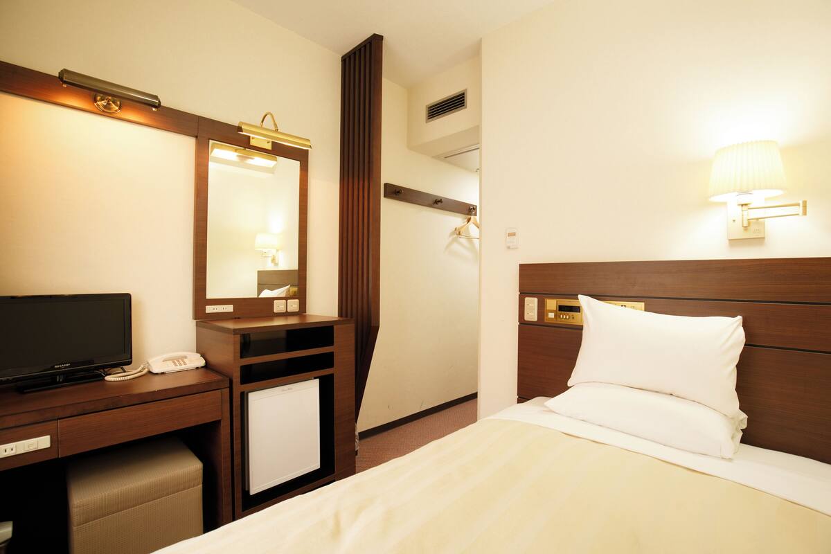 Habitación de hotel con cama, escritorio con televisor, espejo y lámpara de pared.