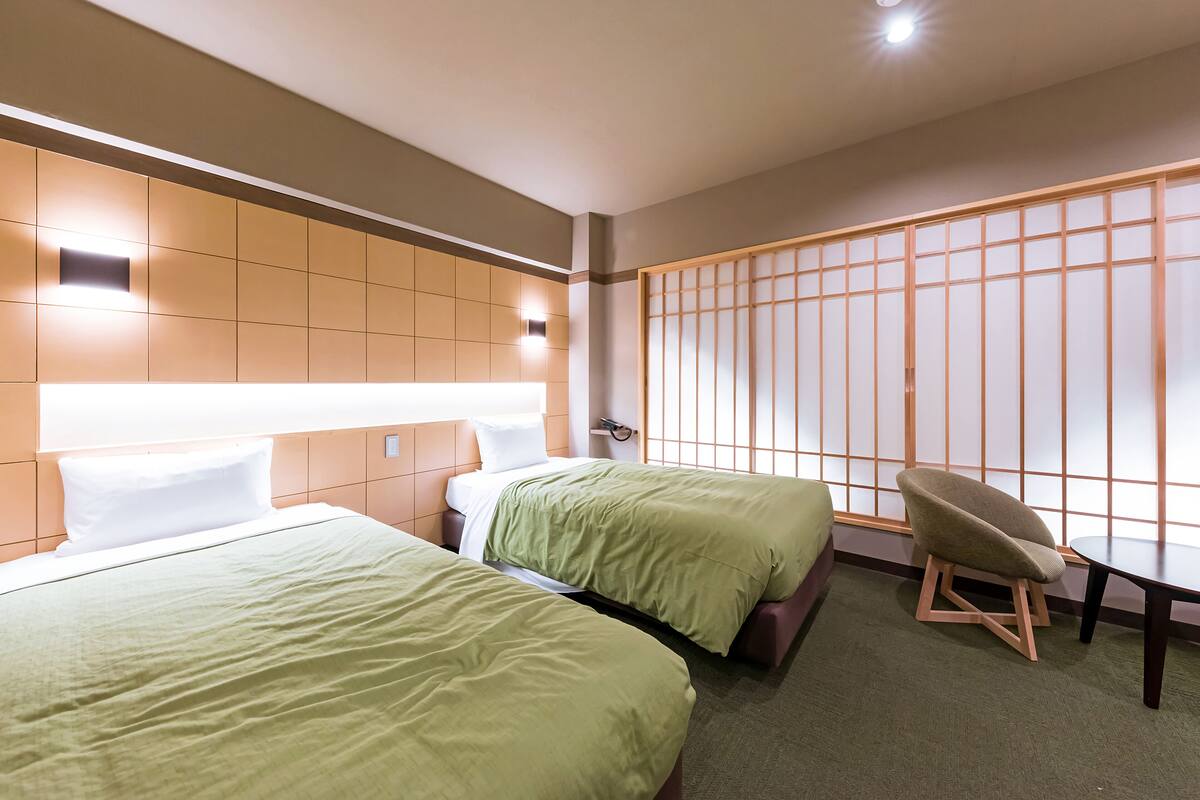 Habitación de hotel con dos camas, una silla, una mesa y un panel shoji.