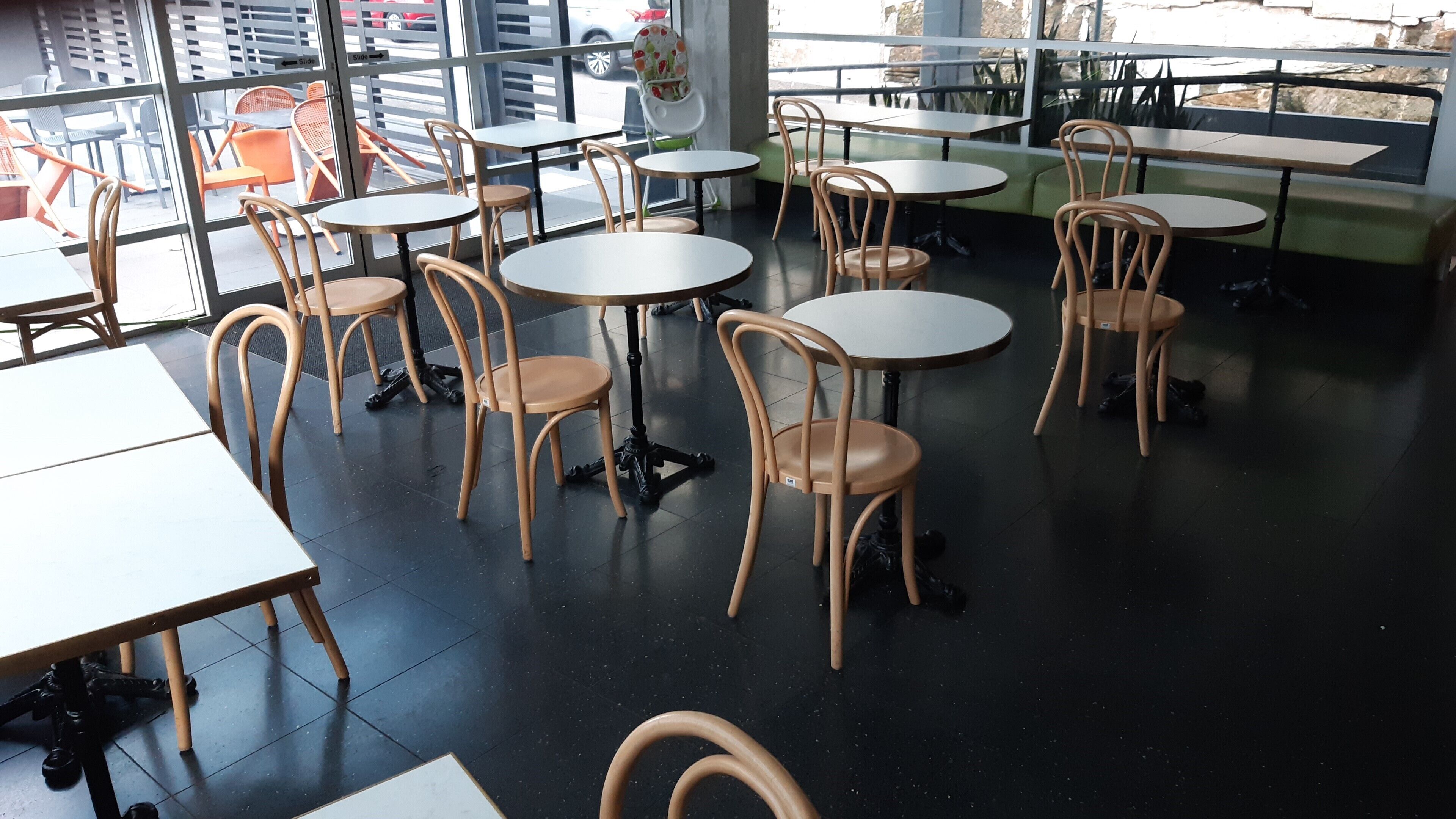 Um café com mesas e cadeiras redondas, grandes janelas e vista para a rua.