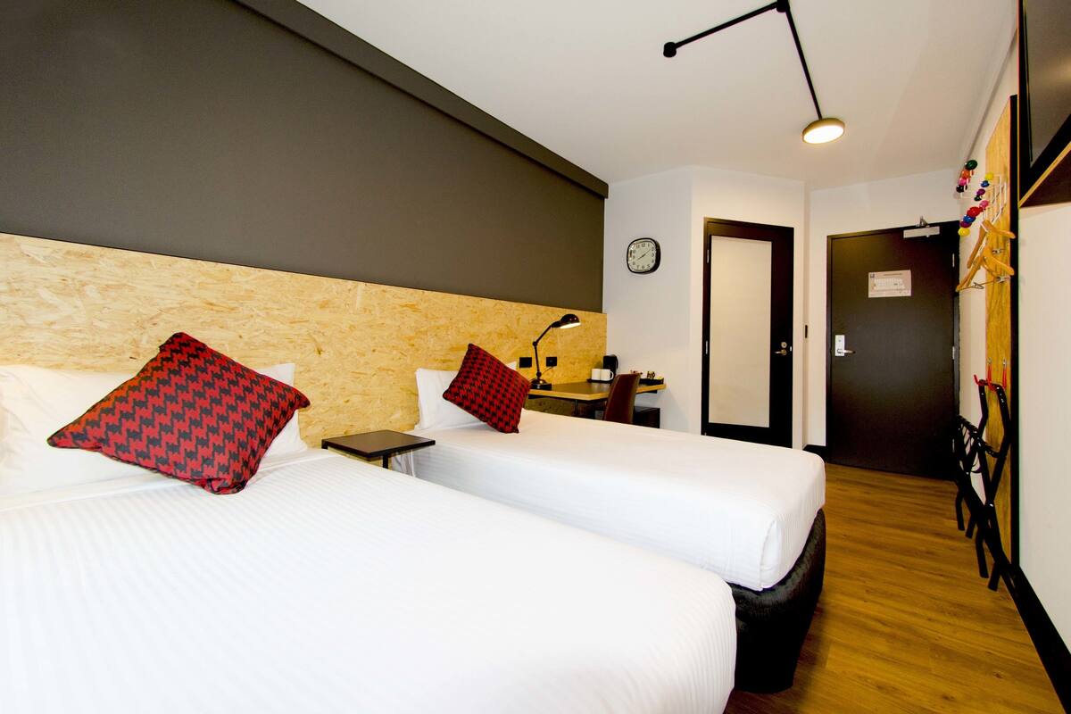 A hotel room with two beds, a wooden headboard, a desk with a lamp, and a bicycle rack.