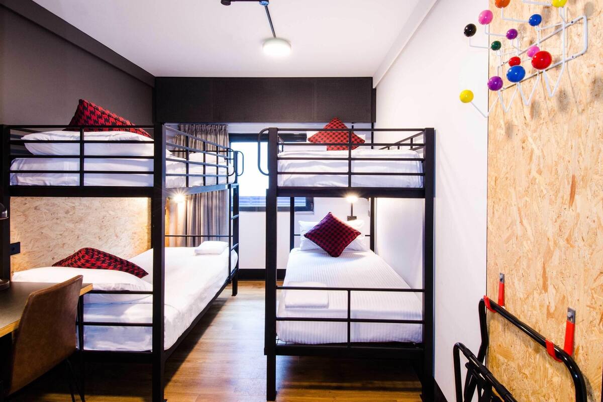 A hostel room with bunk beds, a desk, and a wall-mounted ball rack.