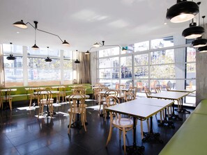Un interior de restaurante con mesas altas, sillas y ventanas grandes.