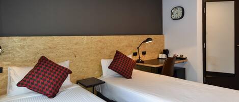 A hotel room with two beds, a desk, a chair, a clock, and a door.