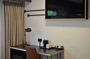 A hotel room with a desk, a chair, a TV mounted on the wall, a coffee maker, and a tray with cups and snacks. - ibis budget Sydney East (Darlinghurst)