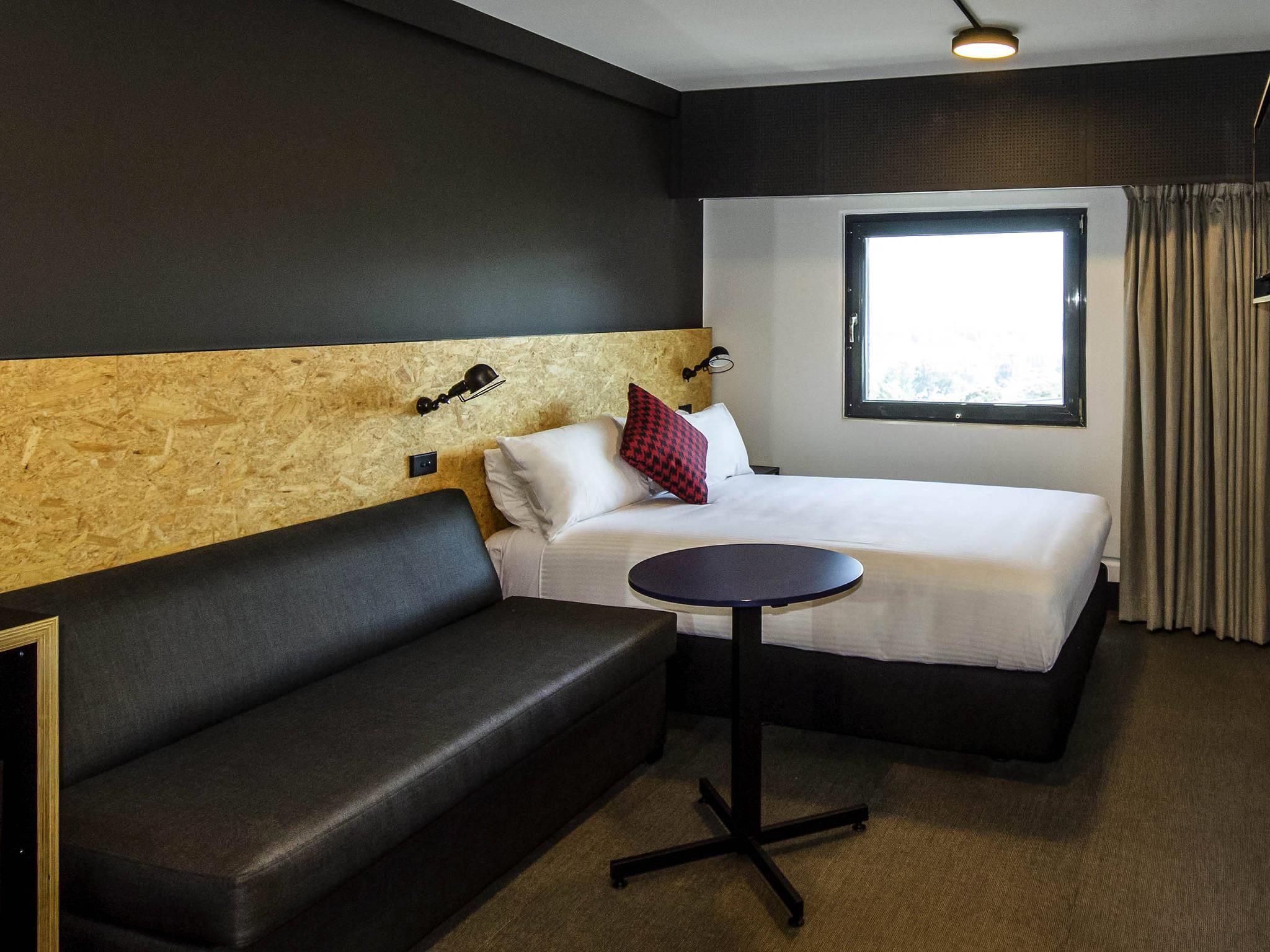 A hotel room with a bed, a small round table, a sofa, and a window with curtains.